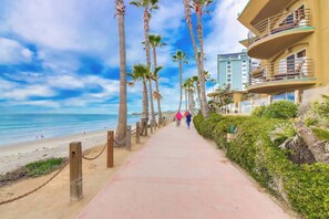 Une promenade en bord de mer, bordée de palmiers, et un immeuble doté de balcons donnant sur l’océan.