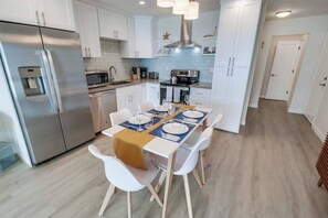 Une cuisine moderne avec des armoires blanches, des appareils en acier inoxydable et un coin repas avec une table dressée pour quatre personnes.