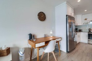 Une cuisine moderne avec un réfrigérateur en acier inoxydable, une table à manger en bois et une chaise blanche, ainsi qu’une horloge murale.