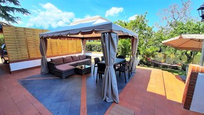 An outdoor patio with a covered seating area, a table, and chairs. - Villa Etna, with swimming pool and garden.  (Blandano)