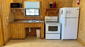 Una cocina compacta con paredes de madera, microondas, estufa, fregadero y refrigerador.