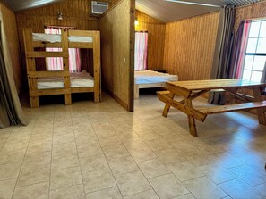 Cozy room with a bunk bed and single bed, featuring a wooden picnic table and a window with curtains.