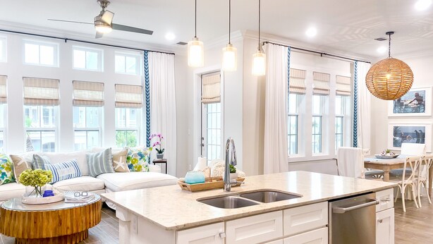 Una cocina moderna con una isla central, armarios blancos, lavavajillas y un comedor con mesa y sillas.