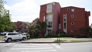 Un edificio de varios pisos con fachada roja, una entrada visible y un paso de peatones enfrente.