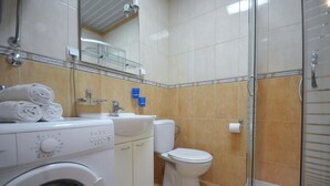 Un baño equipado con lavadora, inodoro y cabina de ducha con mampara de vidrio.