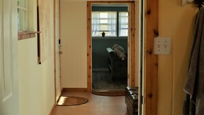 Un couloir étroit aux murs en bois, avec une porte donnant sur une pièce dotée d’une fenêtre et d’un canapé.