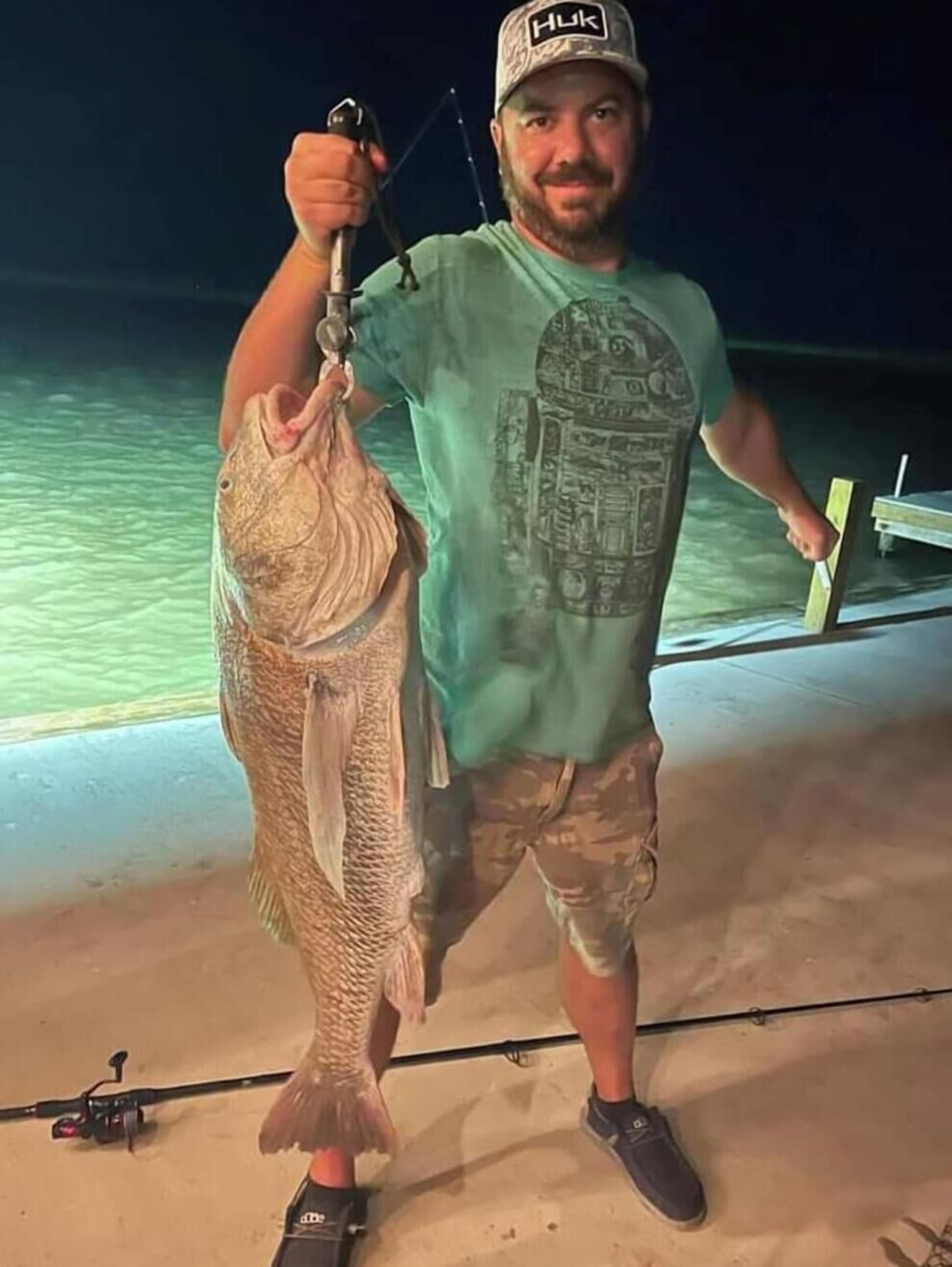 En person holder en fisk og fiskestang på en moler.