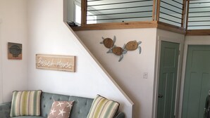 A living room with a green sofa, striped pillows, a 'Beach House' sign, and a wall-mounted turtle decoration.