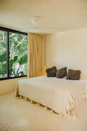 Quarto com uma cama grande, um ventilador de teto e janela com cortinas.
