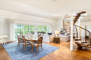 A spacious living area with a dining table, chairs, and a blue rug. A staircase with wooden railings leads to an upper level.