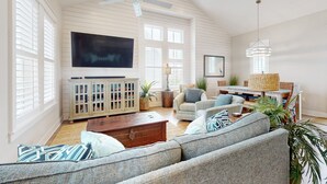 Un salón amplio con un televisor de pantalla plana grande, un ventilador de techo y una zona de estar confortable con un sofá y sillones.