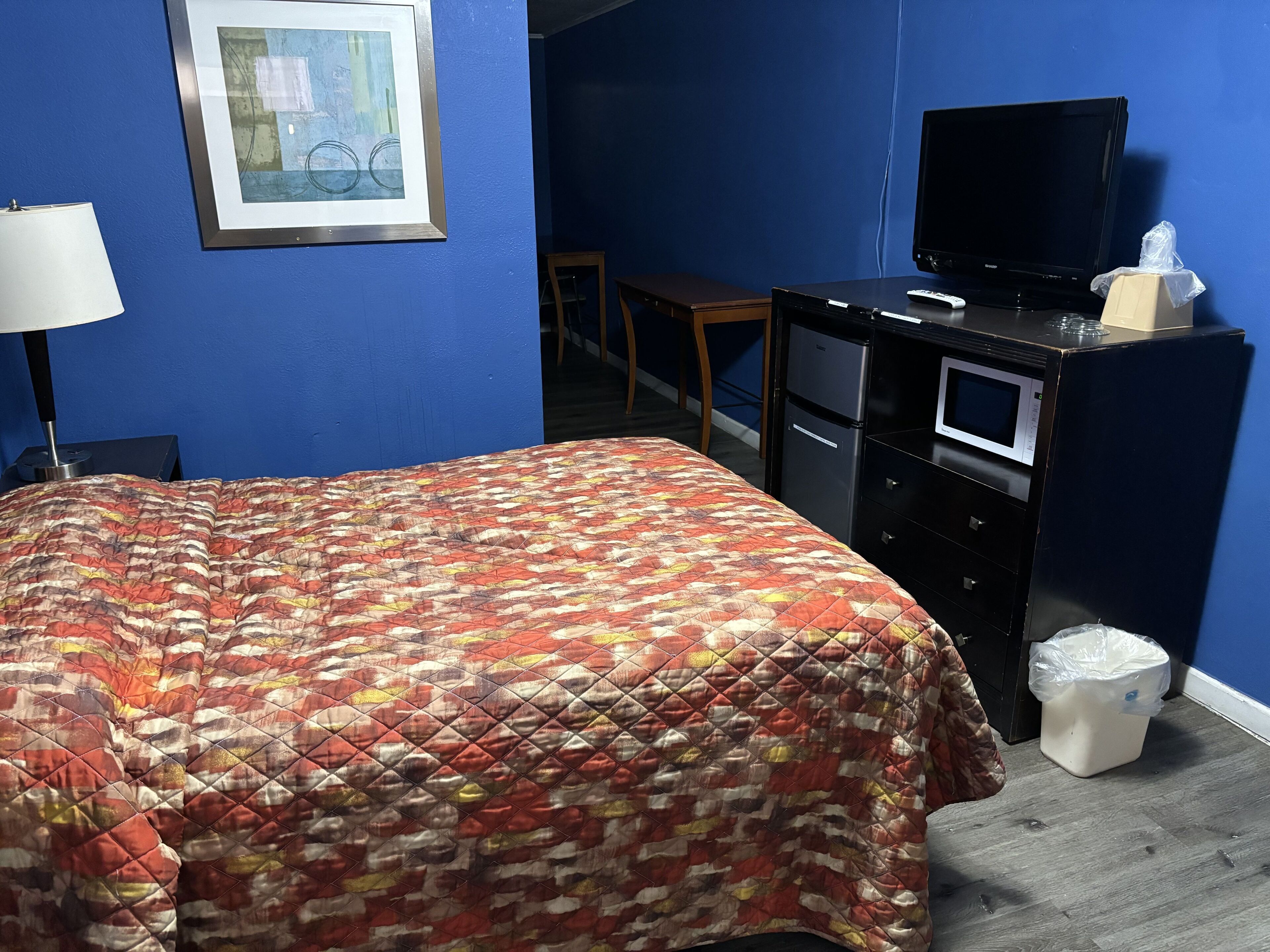 A hotel room with a bed, a desk, a television, a microwave, and a trash bin.