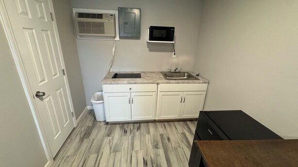 Cocina compacta con armarios blancos, pileta doble, microondas y basurero.
