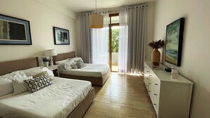 Ein modernes Hotelzimmer mit zwei Betten, einem Schreibtisch und einem großen Fenster mit Vorhängen.