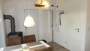 A dining area with a table, chairs, a hanging lamp, a stove, and a coat rack. - Small modern house in the countryside, close to the Schlei and the Baltic Sea (Kappeln)