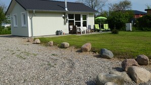A small, single-story building with a sloped roof and a chimney, surrounded by a gravel driveway and a grassy lawn with scattered rocks. - Small modern house in the countryside, close to the Schlei and the Baltic Sea (Kappeln)