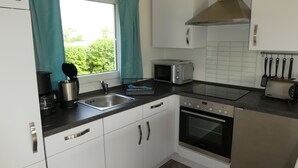 A modern kitchen with white cabinets, a stainless steel range hood, a microwave, a toaster, and a dishwasher. - Small modern house in the countryside, close to the Schlei and the Baltic Sea (Kappeln)