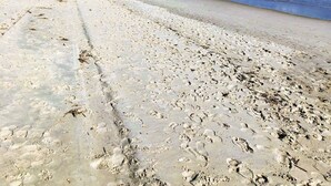 A beach with footprints, a wooden structure, and a view of the ocean under a partly cloudy sky.