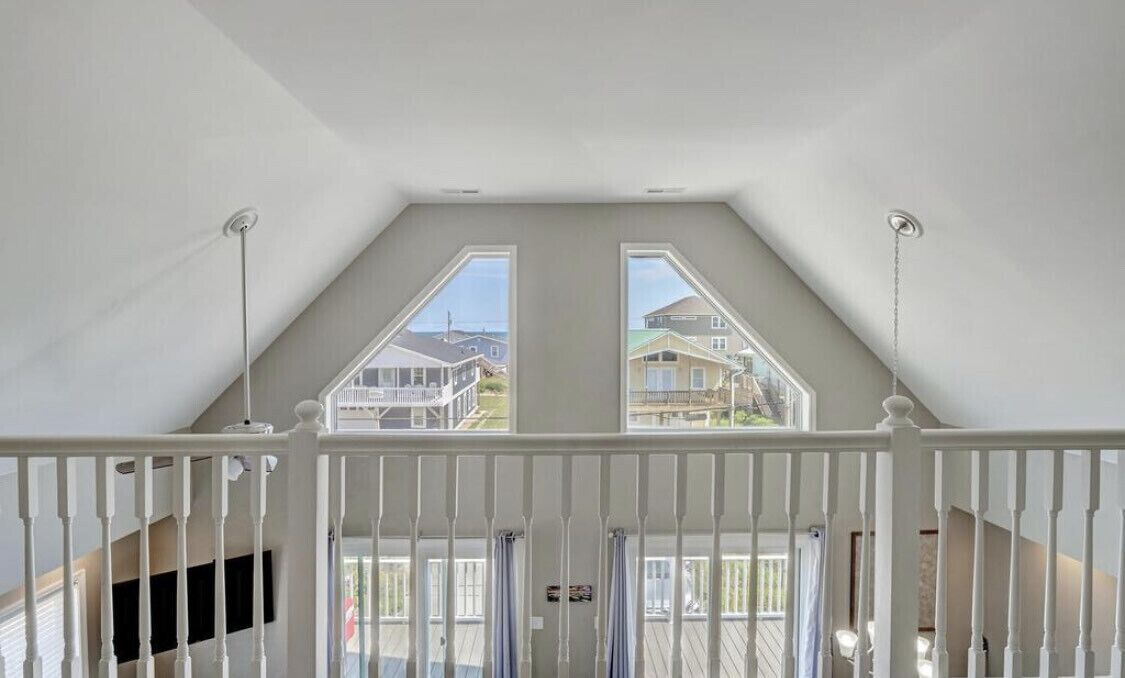 A room with a sloped ceiling and two windows providing a view of neighboring houses.
