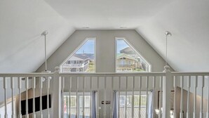 Een kamer met een schuine kap en twee ramen met uitzicht op omliggende huizen.