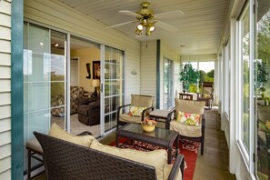Relax on the covered porch with wicker furniture and cushioned chairs, surrounded by glass doors and a ceiling fan.