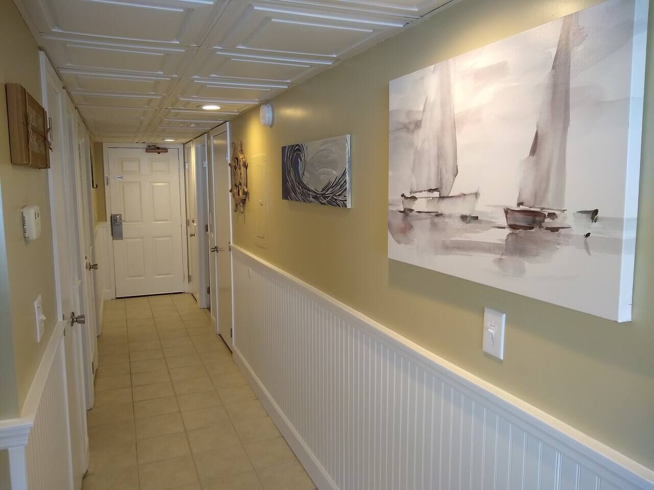 A hallway with white wainscoting, a door at the end, and two paintings on the wall.