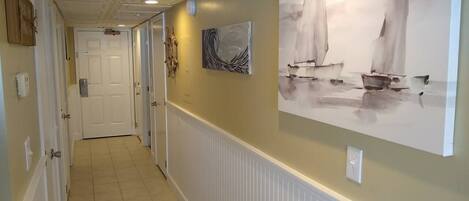 A hallway with white wainscoting, a door at the end, and two paintings on the wall.