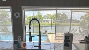 Eine K üche mit großem Fenster, das auf einen Pool und eine Außenbereich-Sitzgelegenheit blickt.