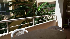 A balcony with a table and chairs, surrounded by large green plants. - Anacasa Dianium Ausias March AP1112 (Denia)