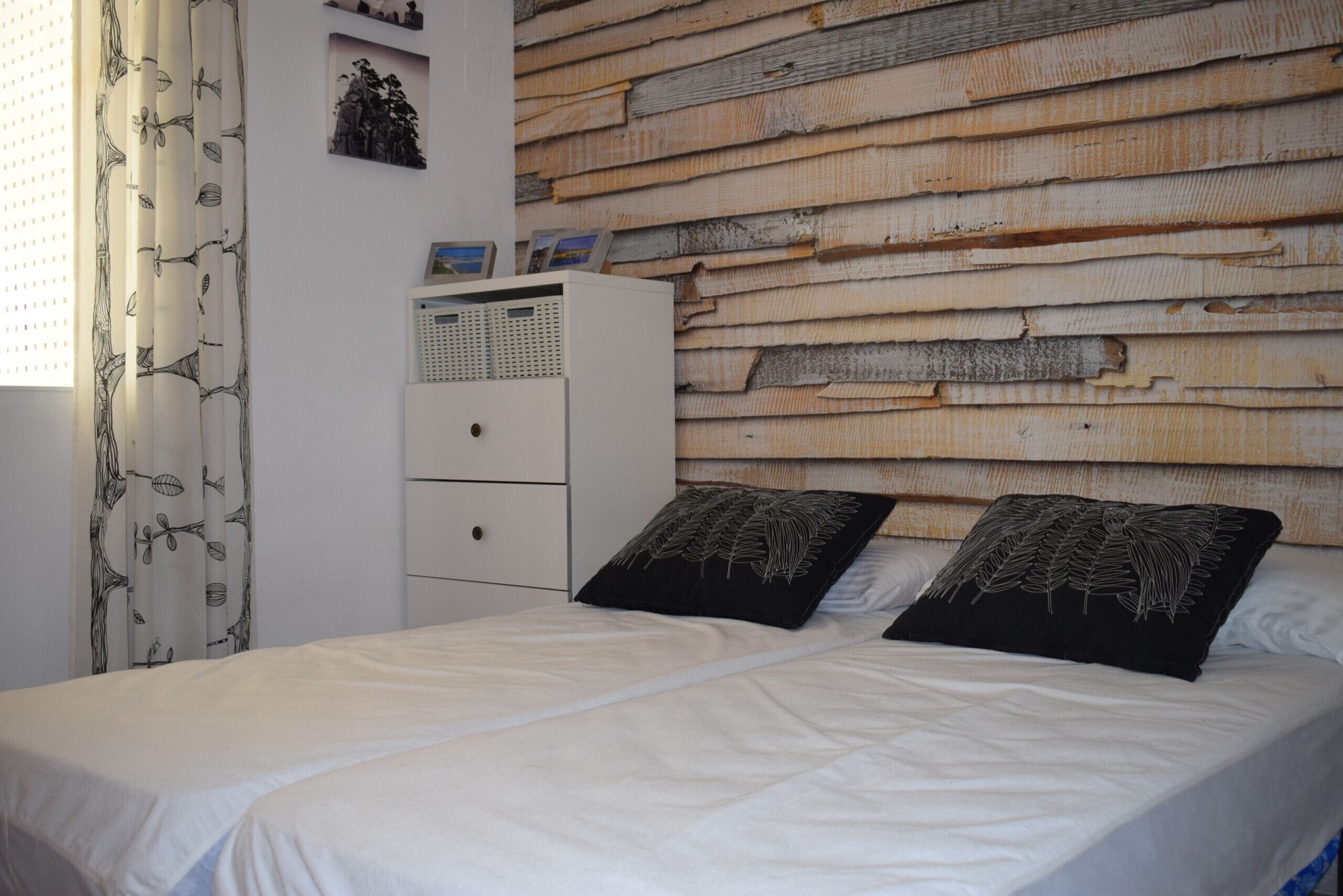 Ein Schlafzimmer mit einem Bett, zwei Kissen, einem Nachttisch, einer Kommode und einer Wand mit Holzpaneelen.