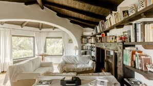 Una habitación acogedora con un sofá blanco, una mesita con un teléfono y una radio, y una estantería llena de libros y objetos decorativos.
