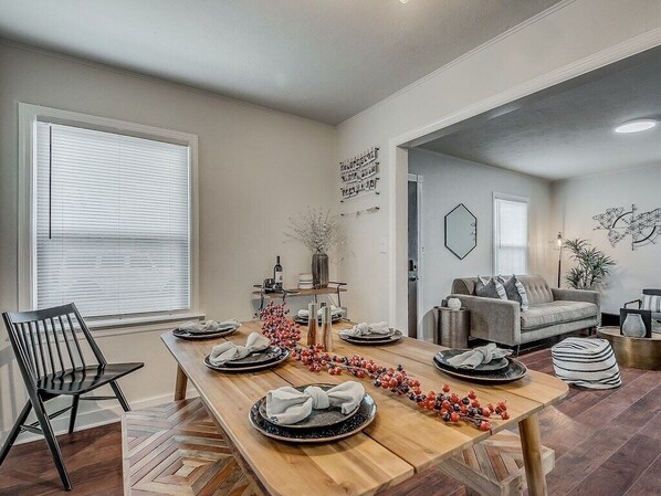 A dining area with a wooden table set for four, a black chair, and a gray sofa in the background.