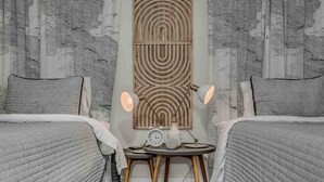 A bedroom with two beds, a wooden table with a clock, and a wall with a geometric pattern.