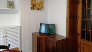 A room with a wooden cabinet, a television on top, a door with glass panels, and a wall with a floral painting. - The house of the Sirolo gecko (Sirolo)