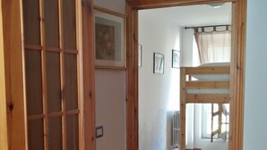 A wooden door with a grid pattern, a hallway leading to a room with a bunk bed, and a radiator on the wall. - The house of the Sirolo gecko (Sirolo)