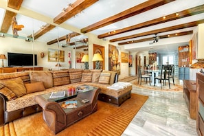 A spacious living room with a large sectional sofa, a glass coffee table, and a dining area with a table and chairs.
