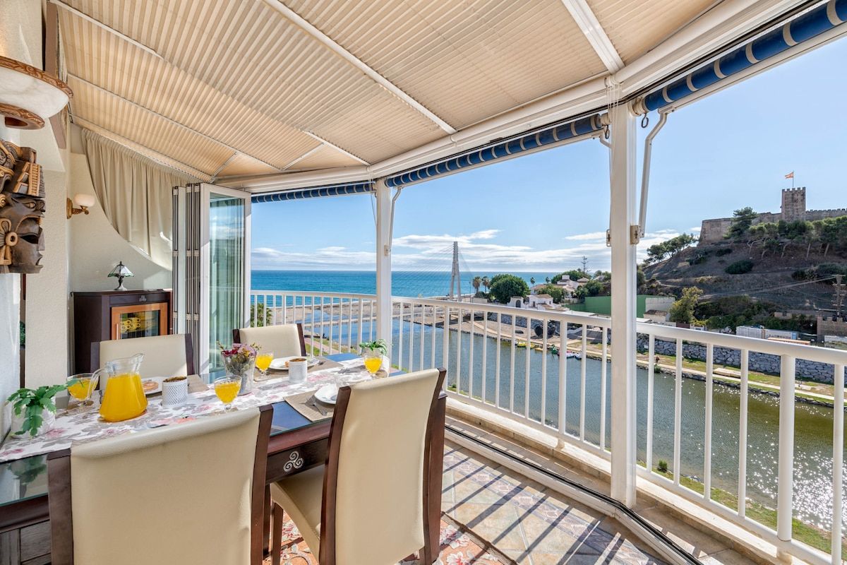 Une terrasse avec une table dressée pour le dîner, offrant une vue sur un plan d’eau et un bâtiment historique.
