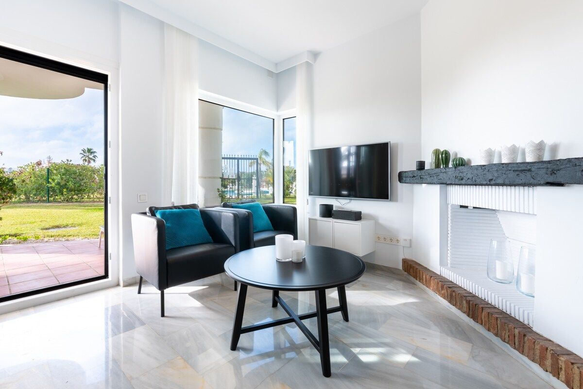 A modern living room with a black sofa, a round table, and a flat-screen TV mounted on the wall.