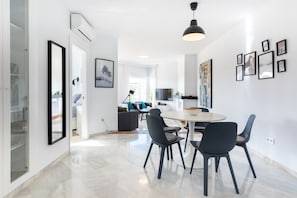 A modern kitchen with a dining area, white walls, and a large window.
