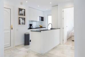 A compact kitchen with white cabinets, a black countertop, and a small trash bin. - Antares I | 2BR Garden & Pool View Apartment in Calahonda Near Marbella (Mijas Costa)