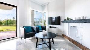 Una sala de estar moderna con un sofá negro, una mesa redonda, un televisor de pantalla plana y una chimenea.