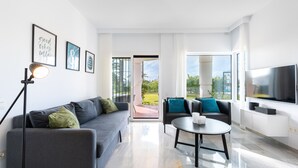 Una sala de estar moderna con un sofá, una mesa de centro y un televisor. Hay cuadros enmarcados en la pared y una puerta que da a un espacio al aire libre.