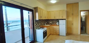 A compact kitchen with a stove, sink, and refrigerator, wooden cabinets, and a view through a sliding glass door.