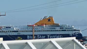 Ein großes Kreuzfahrtschiff mit der Aufschrift 'Blue Star Ferries' am Rumpf, das in einem Hafen vor Anker liegt, mit Stromleitungen und Gebäuden im Hintergrund.