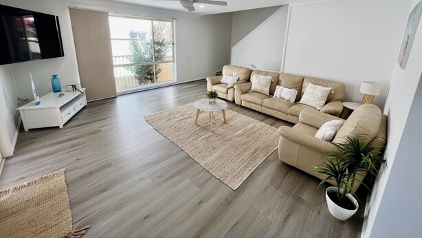 A modern living room with a sofa, coffee table, and a TV mounted on the wall. - House Nelson bay 2min walk to Shops (Nelson Bay)