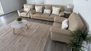A modern living room with a beige sectional sofa, a round coffee table, and a large woven rug. - House Nelson bay 2min walk to Shops (Nelson Bay)