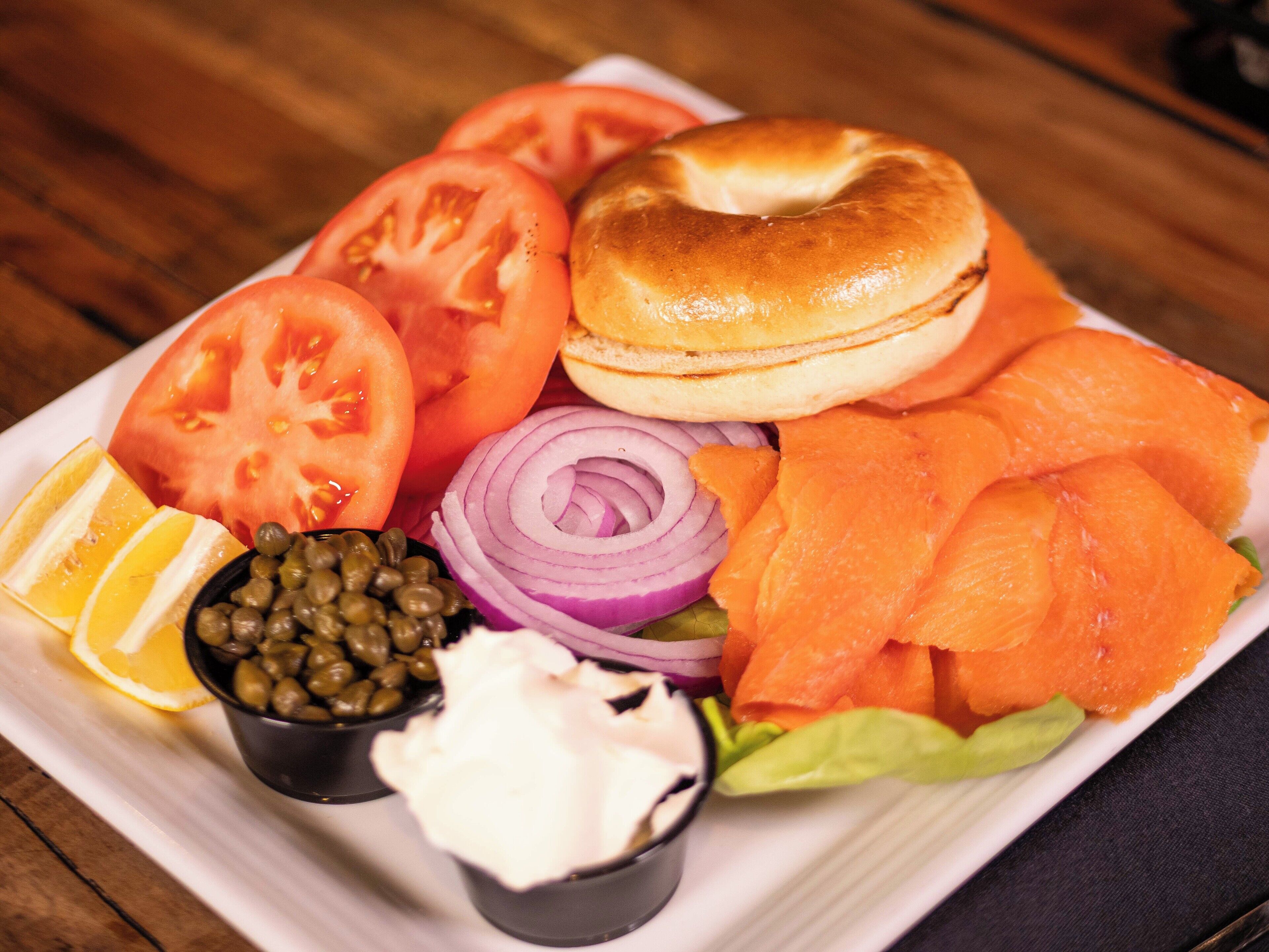 A plate of food with a bagel, smoked salmon, tomatoes, onions, and capers.
