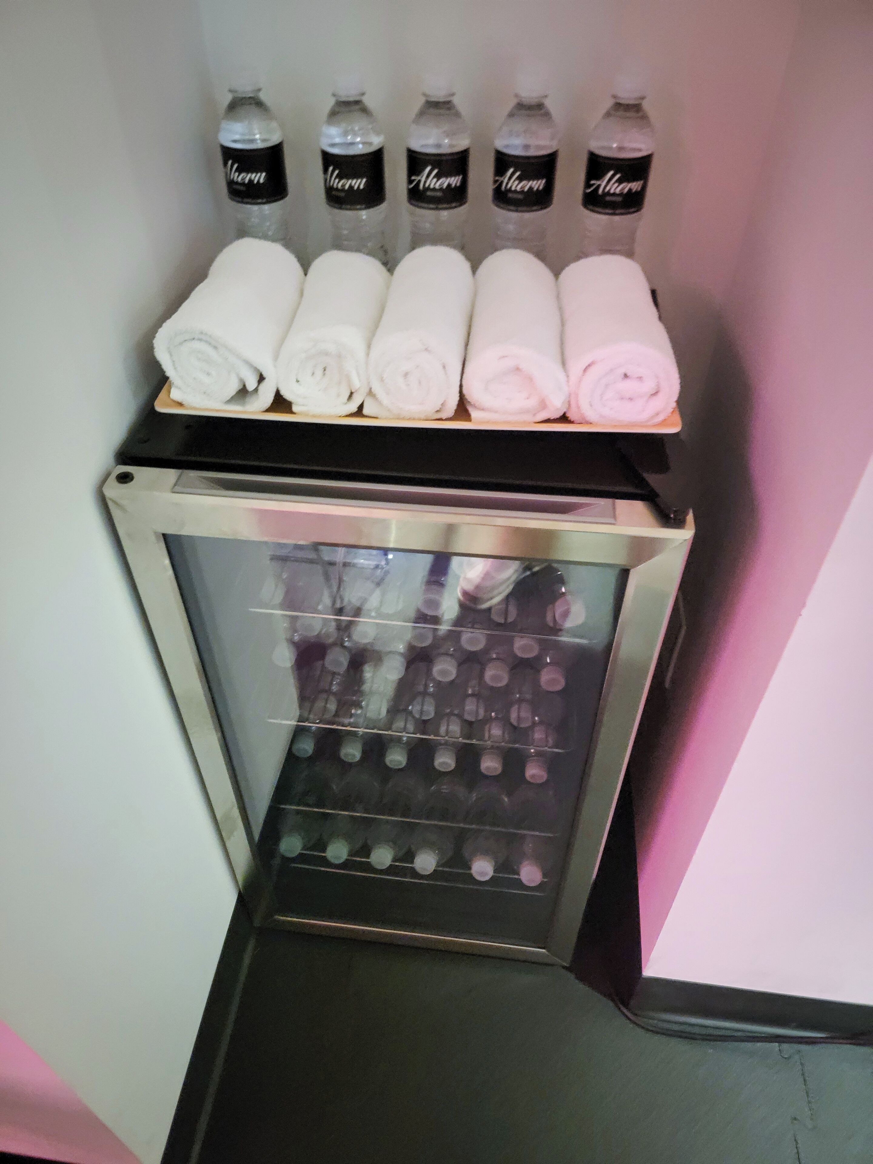 A minibar with bottles of water and neatly rolled towels.