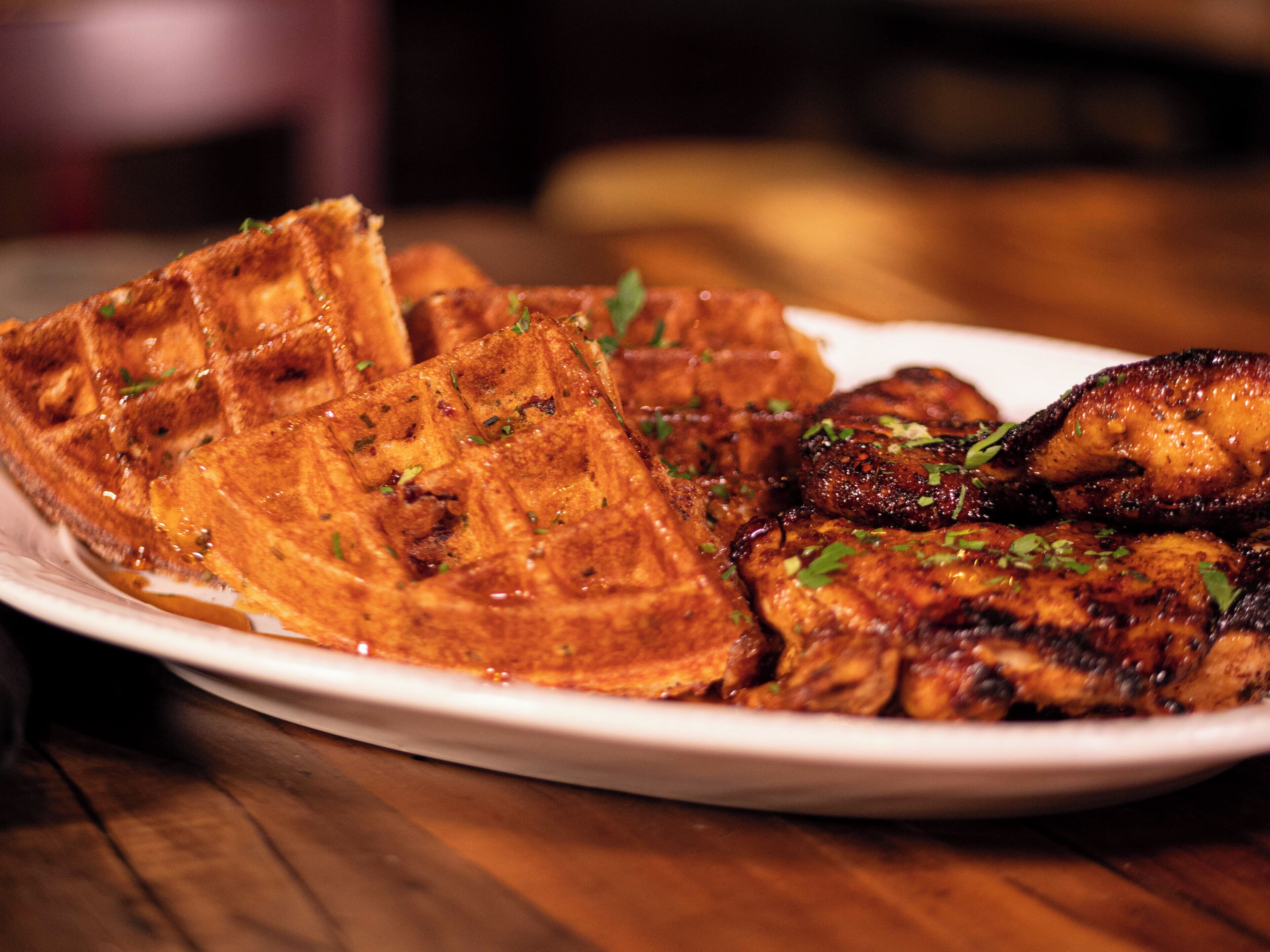 A plate of food with waffles and grilled chicken, garnished with herbs.