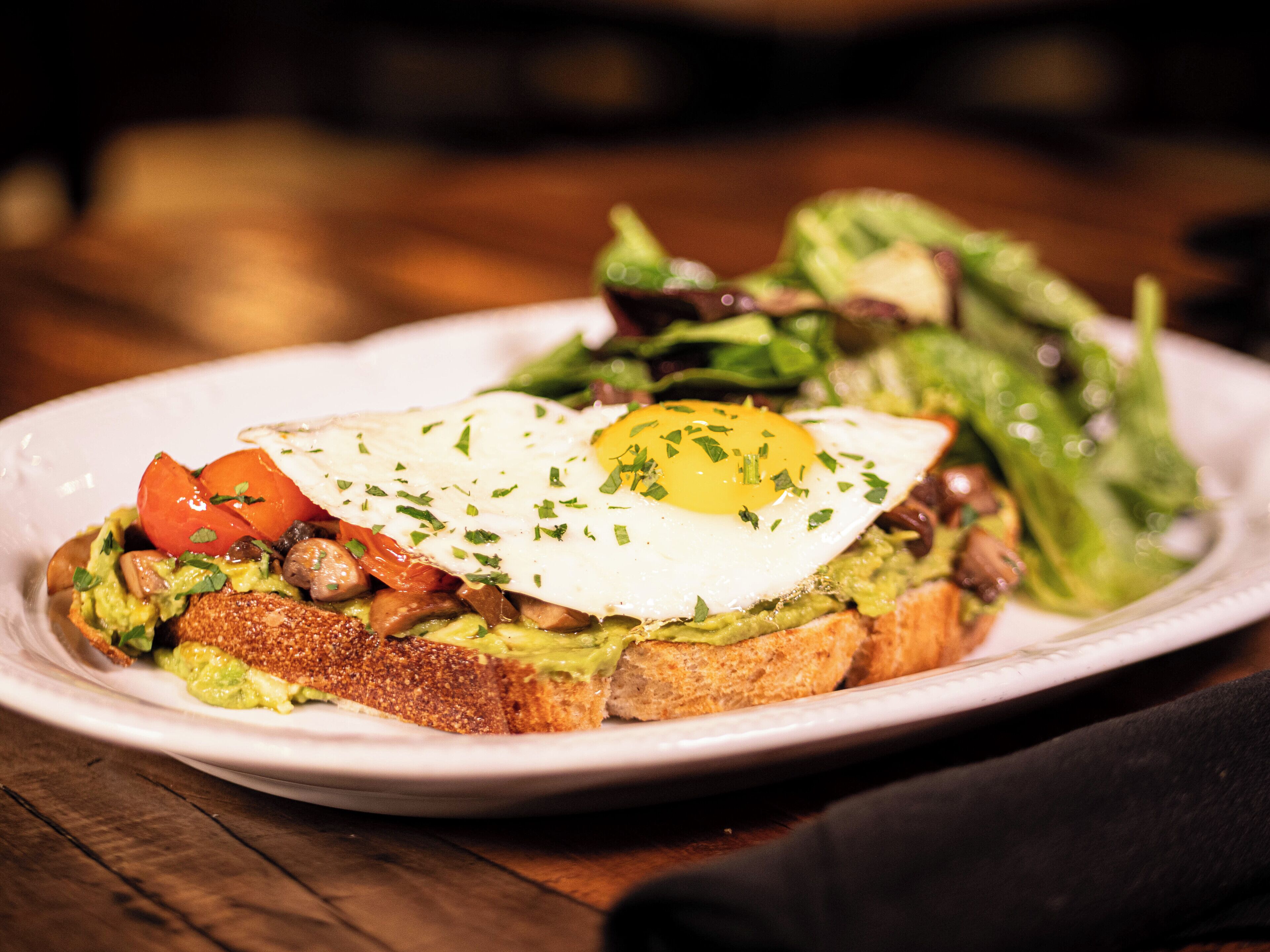 A plate of food with toast, avocado, a fried egg, and vegetables.